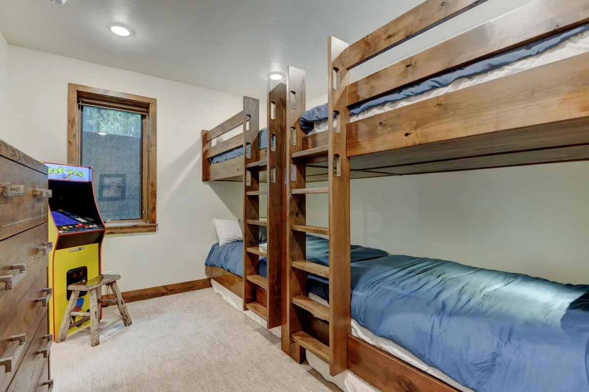 A friendly and inviting bunk room with built-in bunk beds, an arcade game machine in the corner, and sturdy wooden furniture. The setup is playful yet cozy, designed for both restful sleep and fun during downtime.