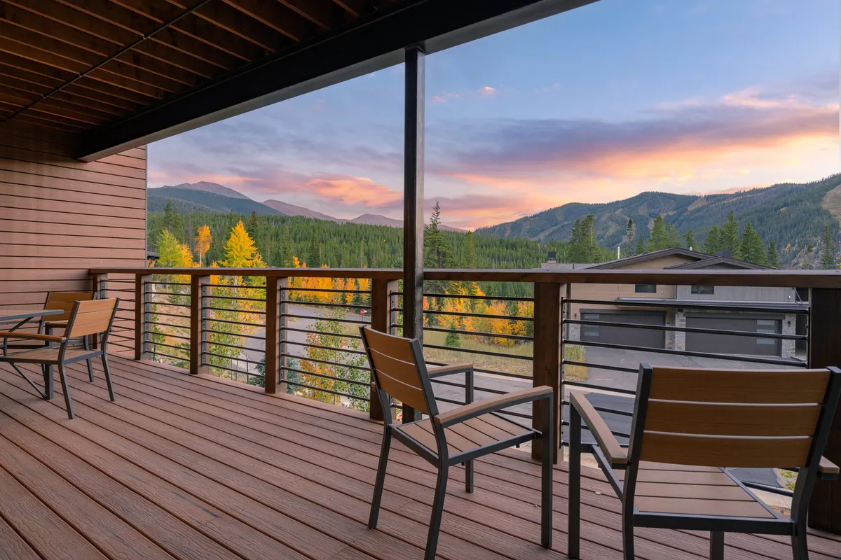 A cozy deck scene with comfortable outdoor furniture, overlooking majestic mountains at sunset. The inviting space suggests relaxation, conversation, and shared moments with loved ones, blending natural beauty with the comforts of home.