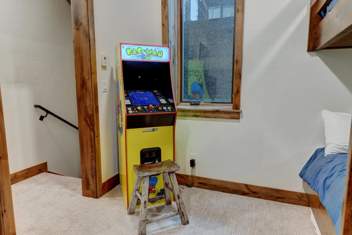 A cheerful interior corner featuring a classic Pac-Man arcade machine and a stool, with a window framing a view outside. The scene suggests playful competition and casual relaxation, inviting kids and adults alike to enjoy nostalgic fun together.