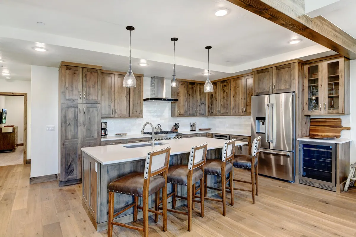 The photo highlights a kitchen with a generous island countertop, stylish stools for bar seating, ample cabinetry, and modern appliances. The layout is open, fostering social interaction and culinary creativity.