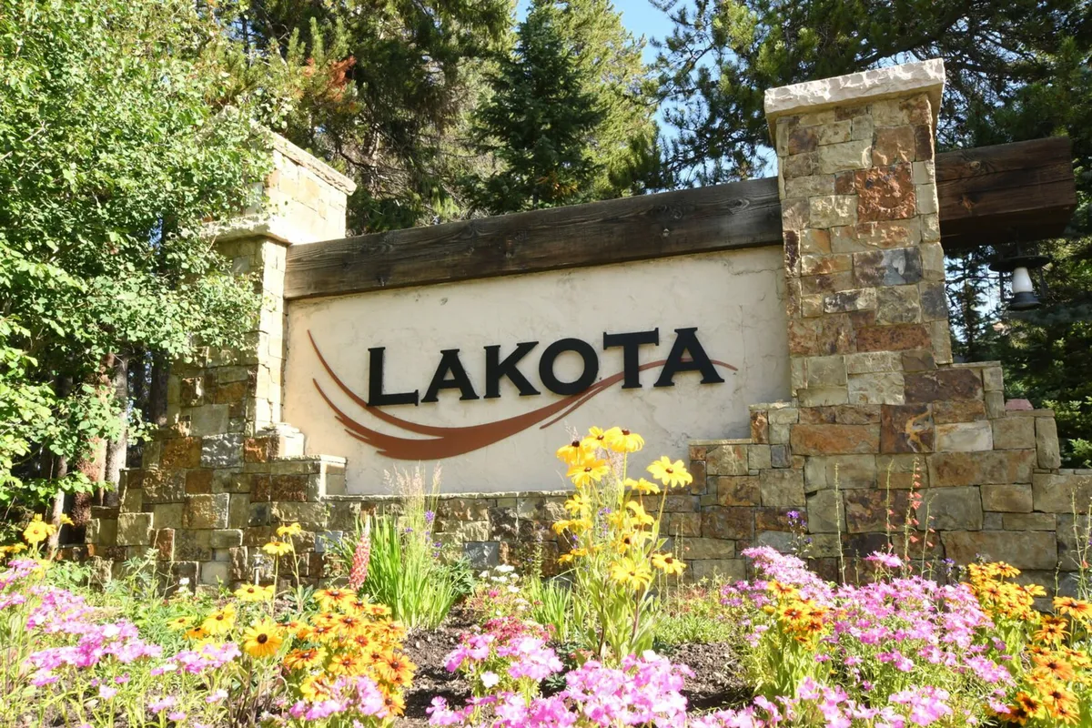 The welcoming entrance to the Lakota area, marked by a prominent 'LAKOTA' sign, lush flower beds, and stone pillars, inviting visitors to explore scenic surroundings and appreciate the mountain setting.