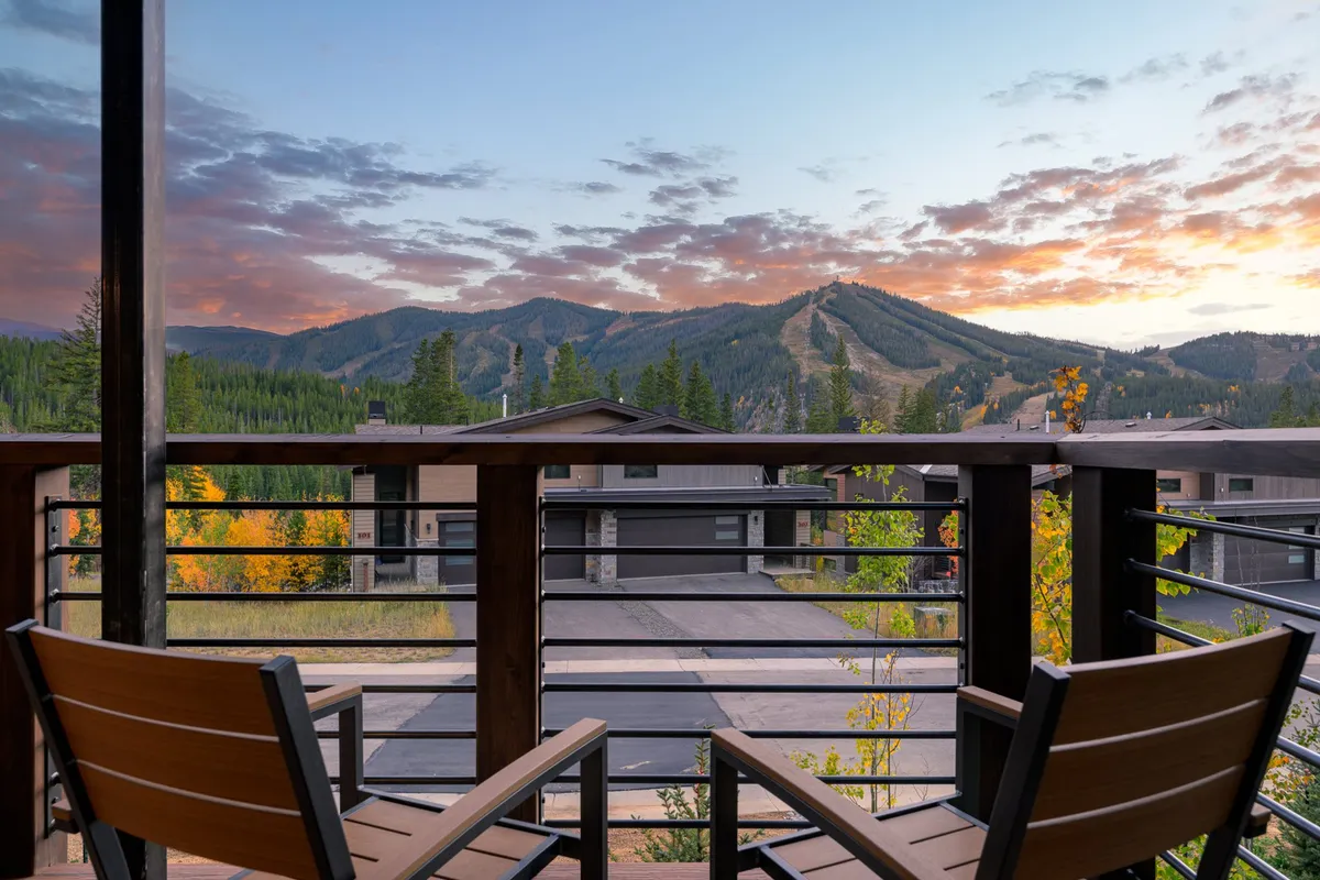 A tranquil view from a balcony with comfortable chairs, looking out over a breathtaking mountain range beneath a vibrant sunset sky. The setting invites moments of relaxation, reflection, and appreciation of the landscape.