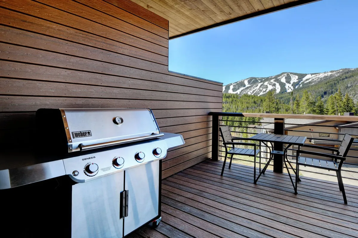 An outdoor dining space featuring a grill, table, chairs, and an expansive mountain vista. The warm lighting and inviting setup encourage communal meals and socializing outdoors, reinforcing the idea of shared experiences in a beautiful setting.